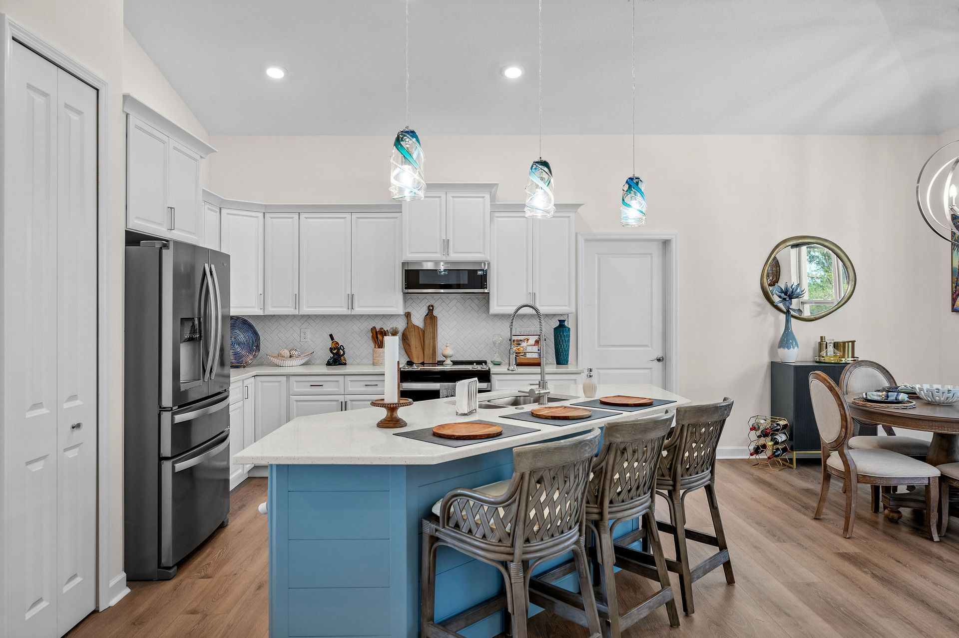 Kitchen with white cabinets, blue island, pendant lights, and wood flooring.